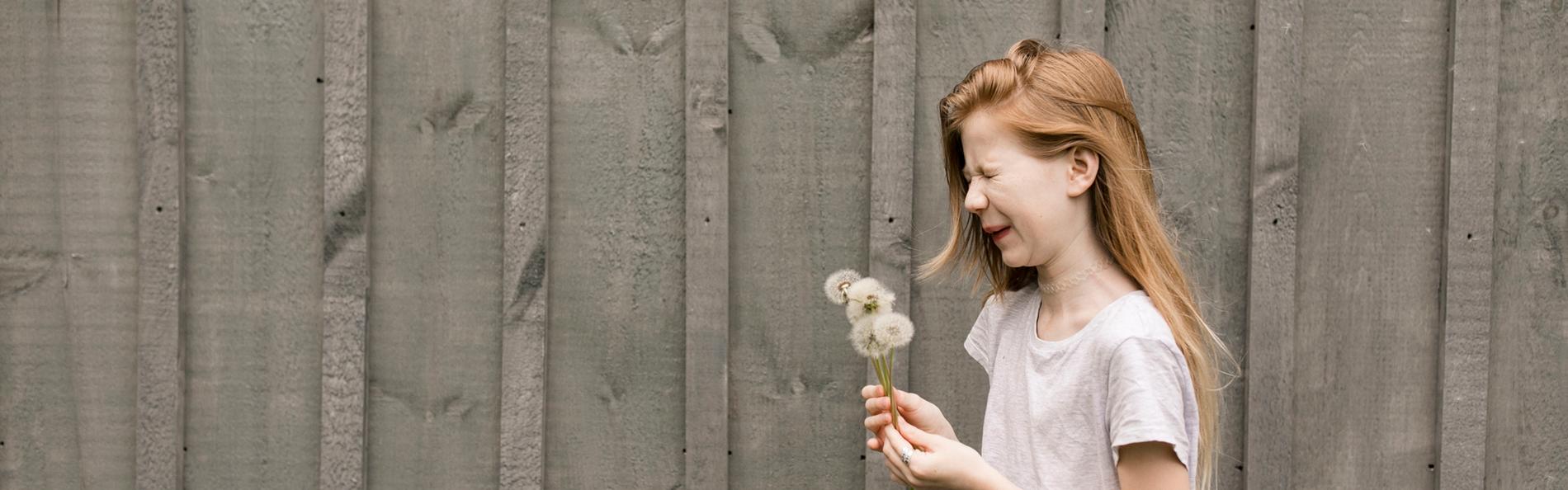 Mädchen mit Pusteblume vor Zaun