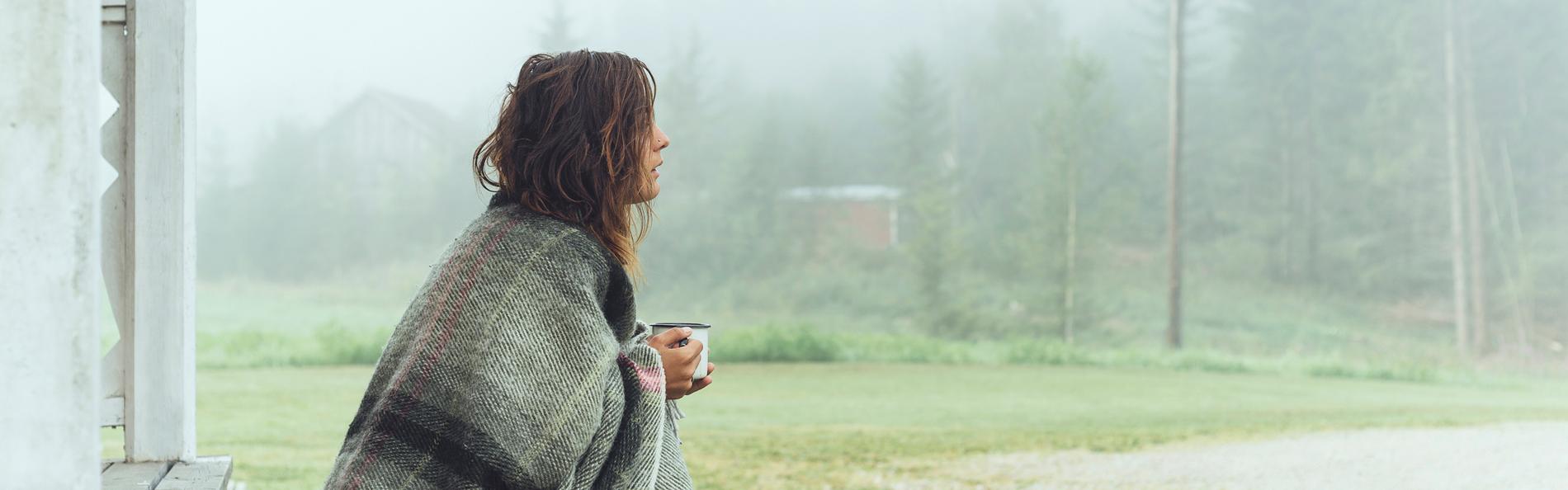 Frau mit Decke trinkt Kaffee im Nebel