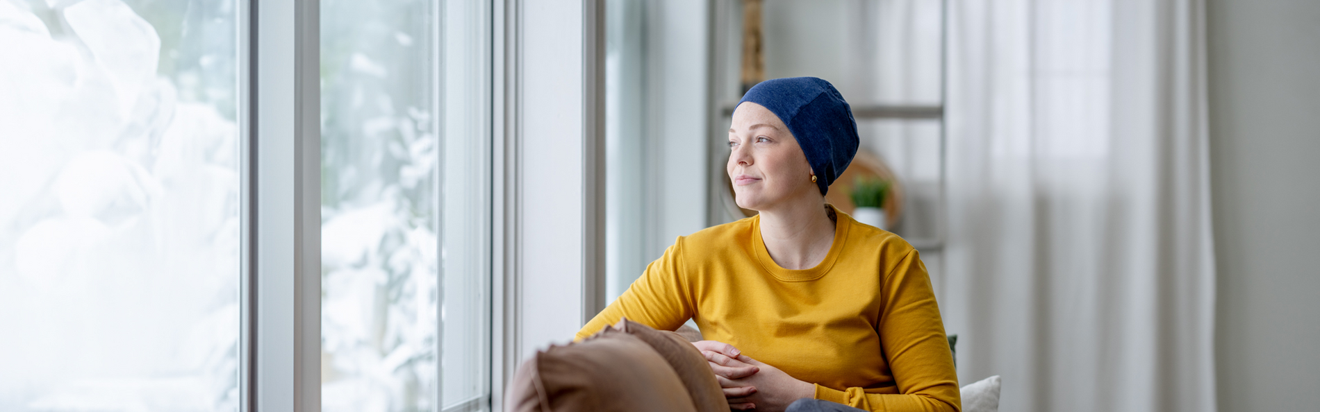 Junge Krebspatientin sitzt am Fenster