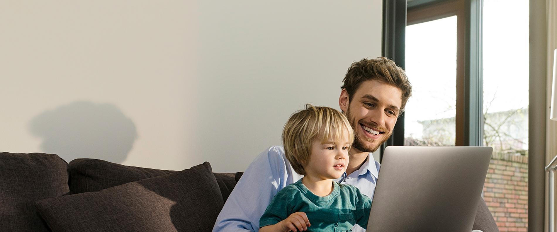 Mann mit Kind auf dem Schoß schauen in den Laptop 