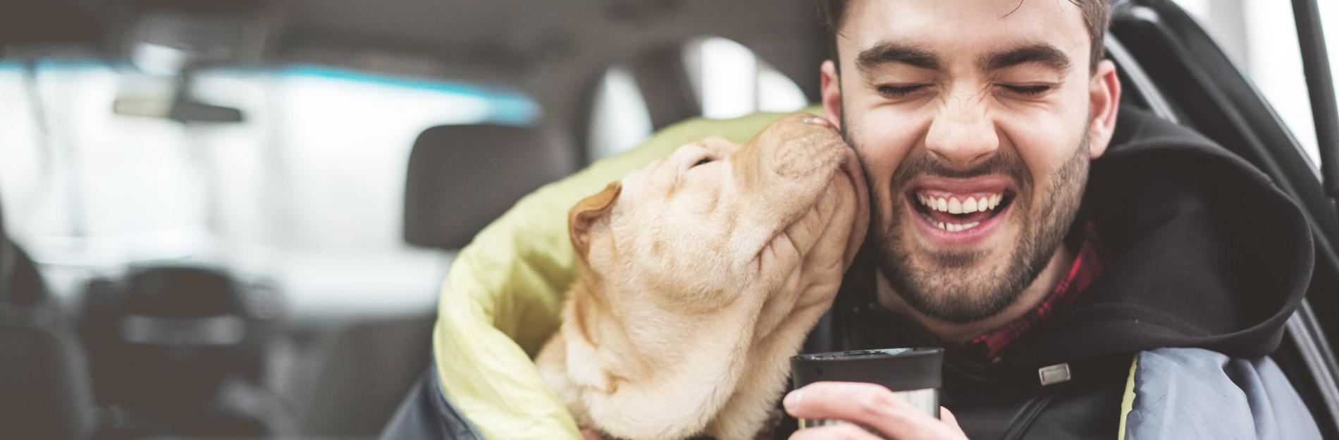 Mann sitzt mit Hund unter Decke und trinkt Tee