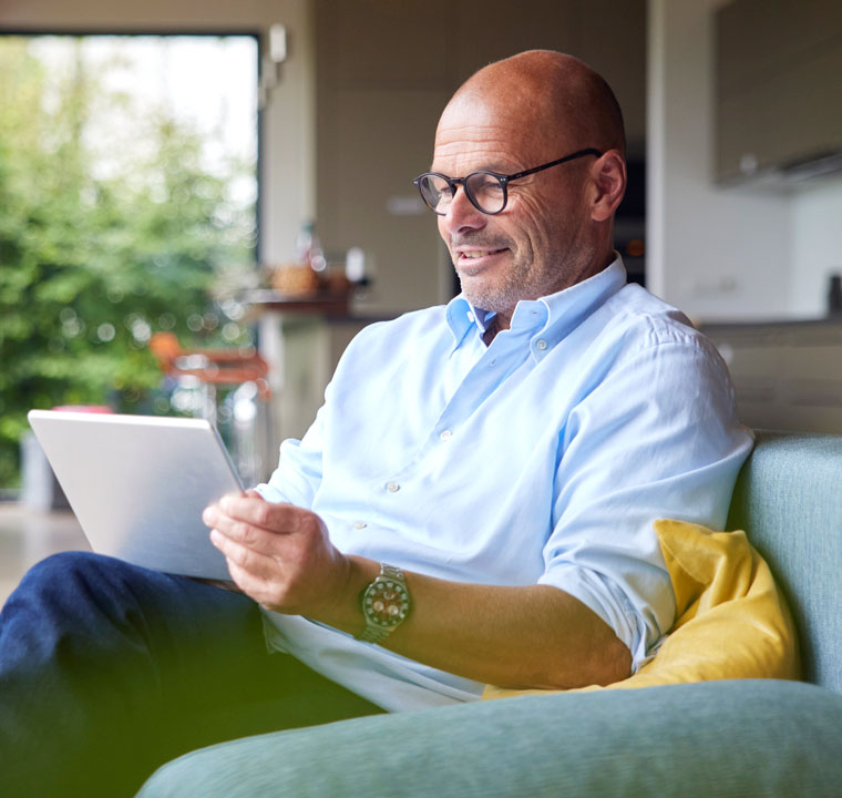 Älterer Mann sitzt auf Couch und schaut auf sein Tablet
