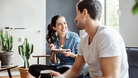 Junges Paar sitzt kuchenessend auf Sofa