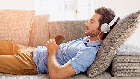 Mann mit Kopfhörern liegt auf Couch