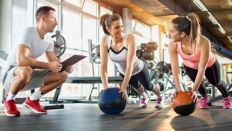 Zwei Frauen trainieren im Fitnessstudio mit Ihrem Trainer