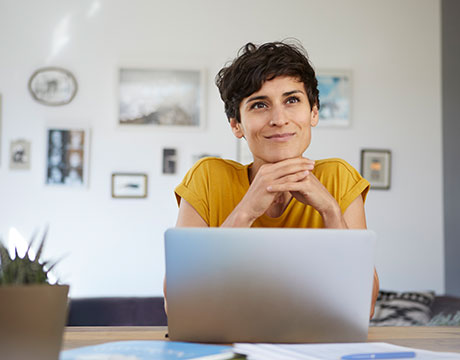 Frau mit gelbem Pulli sitzt vor ihrem Laptop