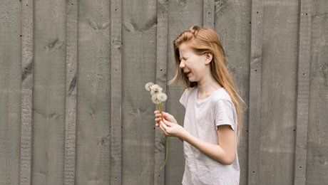 Mädchen mit Pusteblume vor Zaun