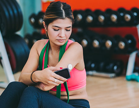 Junge Frau sitzt im Gym und liest Diabetes Daten aus