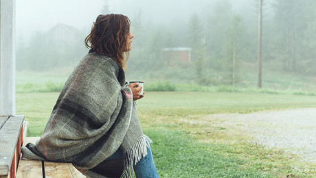 Frau mit Decke trinkt Kaffee im Nebel