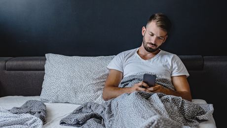 Mann nutzt Smartphone im Bett